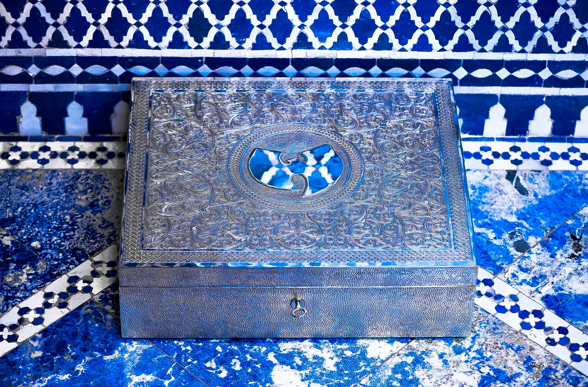 An ornate silver box with the Wu-Tang "W" logo resting on a blue and white marble counter.