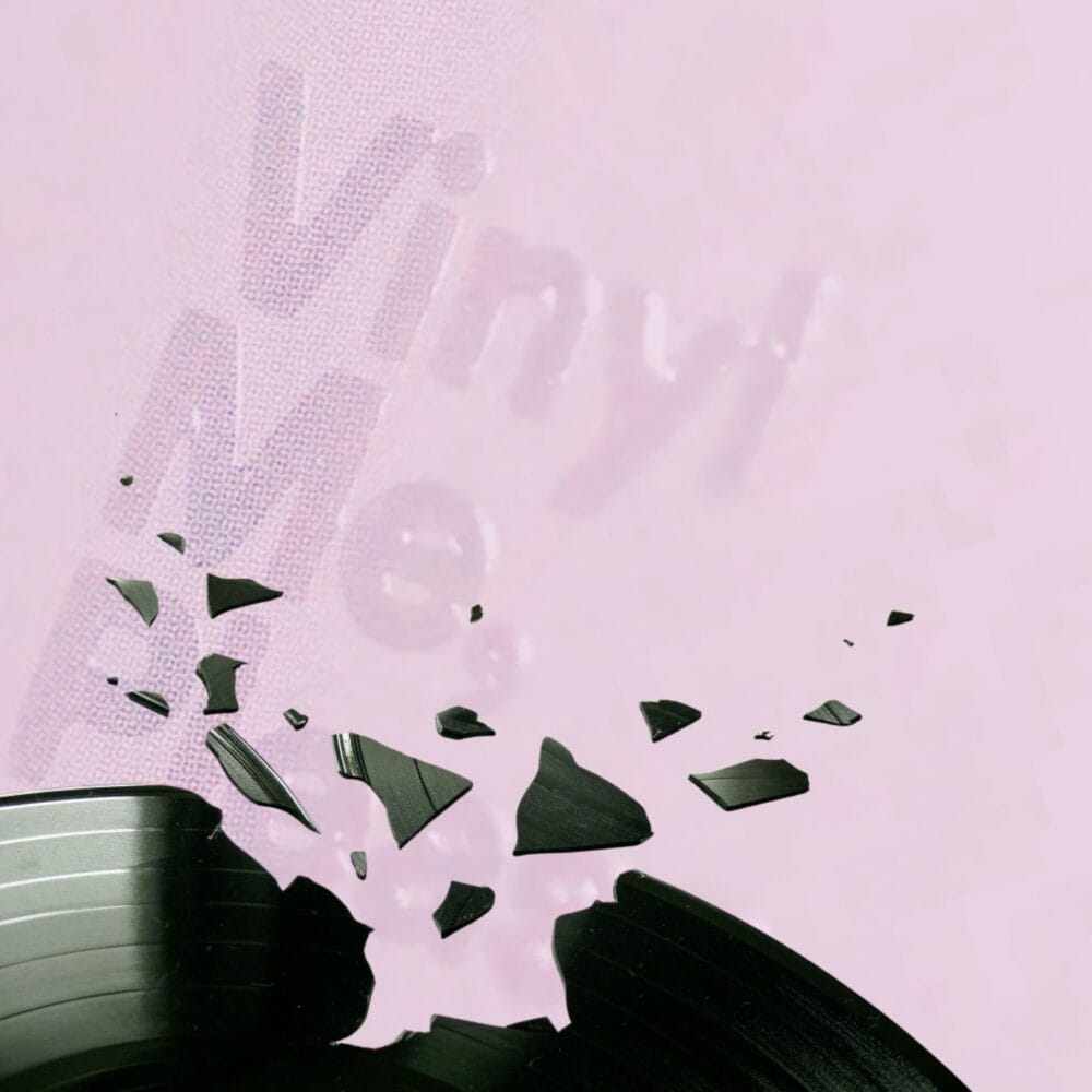A broken record with "Vinyl Me Please" please faintly behind it on a pink background.