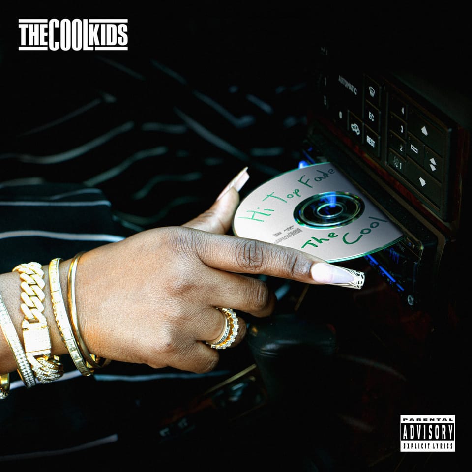 The cover for The Cool Kids "Hi Top Fade". A dark-skinned hand inserting a CD into a car's CD player. The hand is adorned with gold jewelry, including on the tips of long acrylic nails.