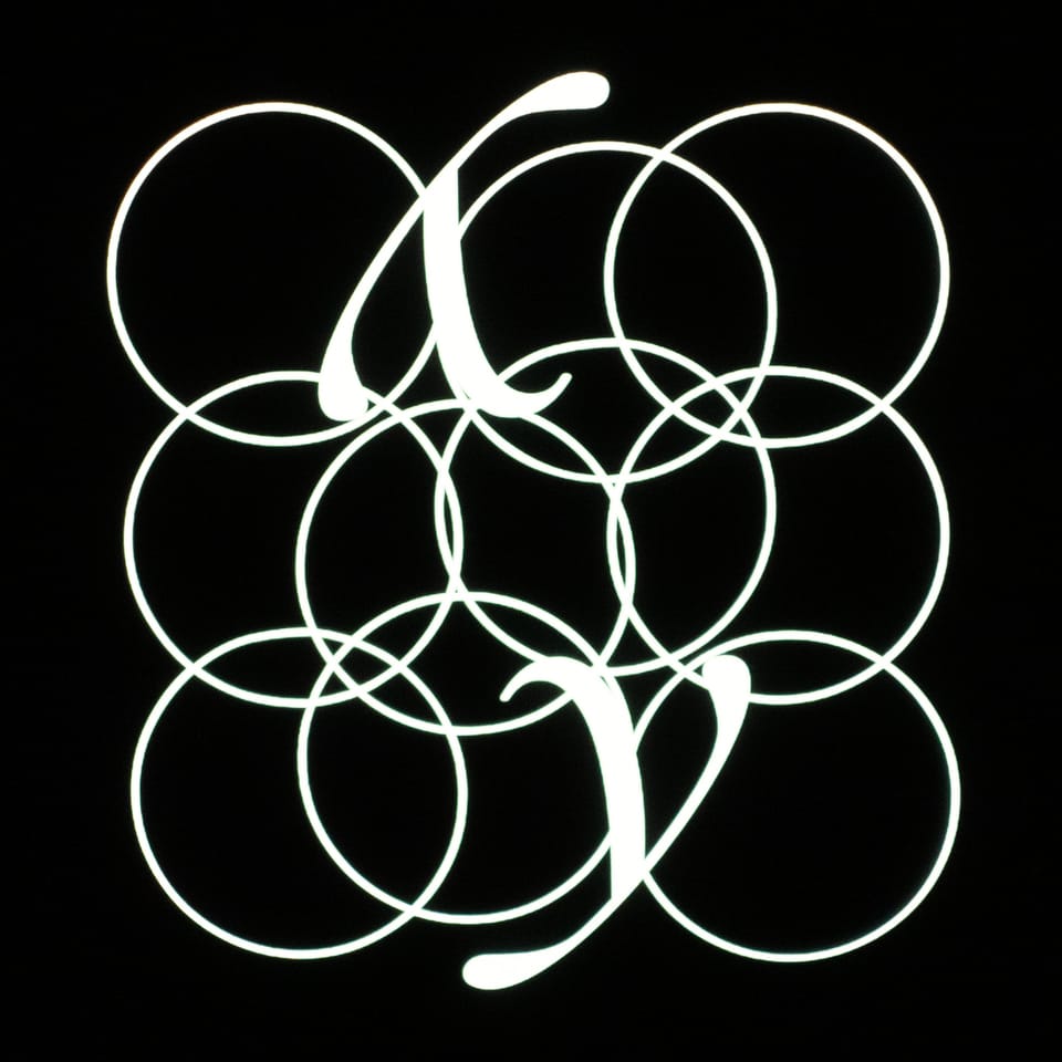 The cover of "My Ghosts Go Ghost", 10 interlinked circles and two Y's (one rightside up, the other upside down) in white over a black background.