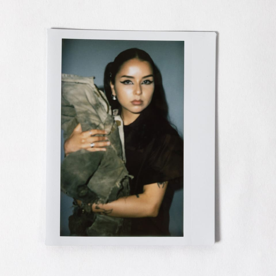 A blurry poloroid of Lexa Gates cradling a bundle of denim. The poloroid is laid on a white background.