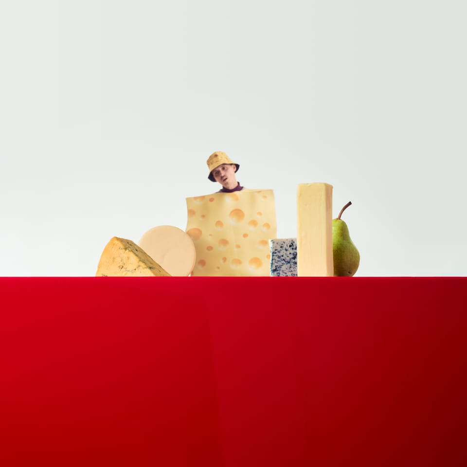 A square with white on the top half and red on the bottom. An assortment of cheeses (and one pear) are arranged on the dividing line. NAHreally's head sticks out of the cheese in the center.